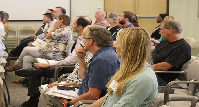 A group of participants from the Southern California Bight 2018 Regional Monitoring program sit in chairs in a SCCWRP conference room listening to a presentation.